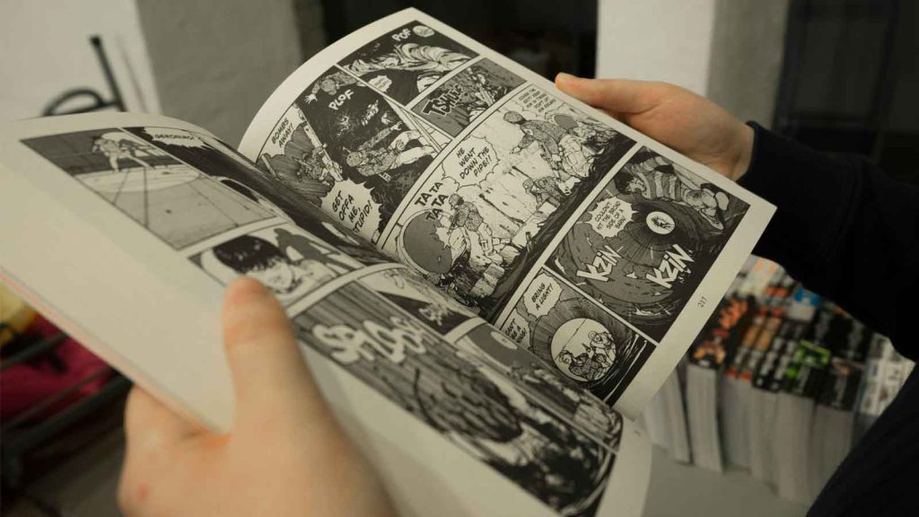 A person holding an open manga book in black and white.