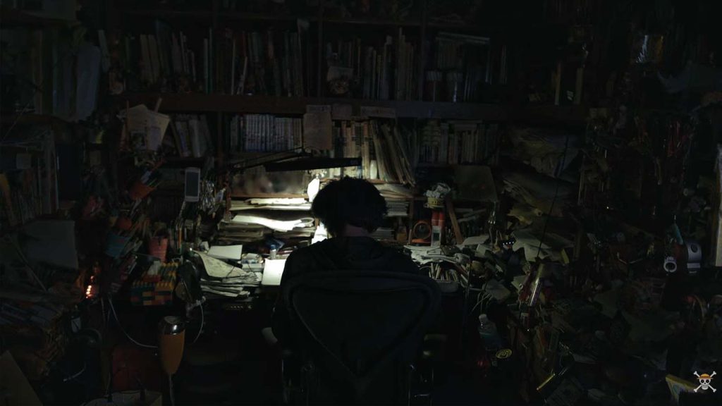 One Piece creator Eiichiro Oda's workstation. The image shows Oda working on a table with a lamp in front of him.