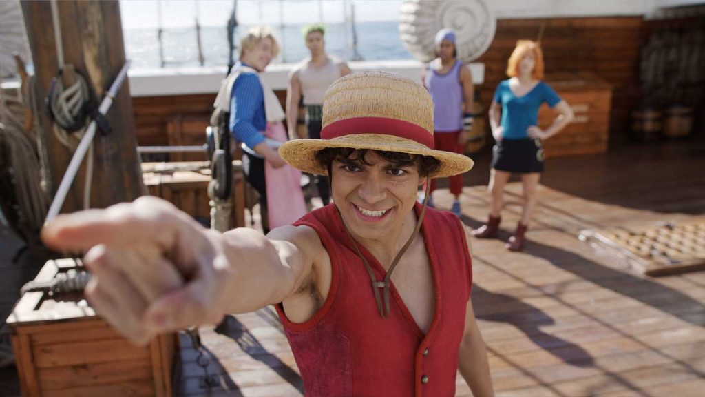 The main characters of One Piece live action season 2, showing Inaki Godoy as Monkey D. Luffy smiling while pointing to a direction aboard a ship. Behind him are the rest of the Straw Hats Taz Skylar as Sanji, Mackenyu Arata as Roronoa Zoro, Jacob Romero as Usopp, and Emily Rudd as Nami.