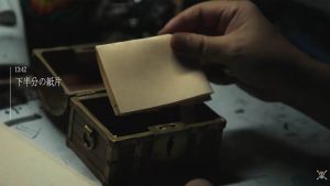 A close up of Eiichiro Oda's hand as he puts a piece of paper inside a treasure box.