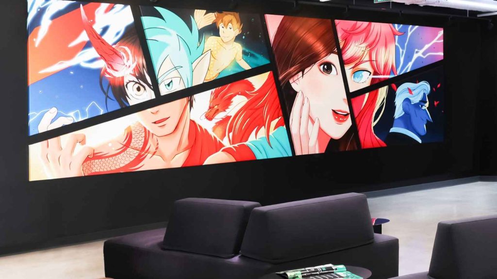 A look at the Webtoon office space, showing black sofas and a collage of titles available on the platform.