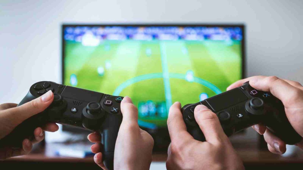 Two people holding Playstation controllers playing a soccer game on television in the living room