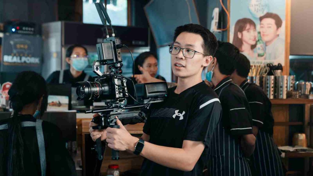 An Asian cameraman holds a camera during filming and is leaning backwards