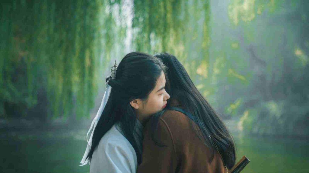 Asian women embracing each other at the side of a pond with natural vegetation in the background