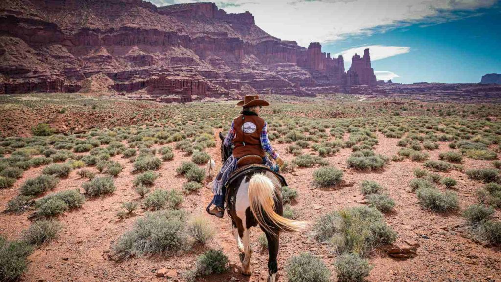 A modern cowboy riding a horse near  near Fisher Towers Castle Valley, Utah where the land is barren against a rocky landscape