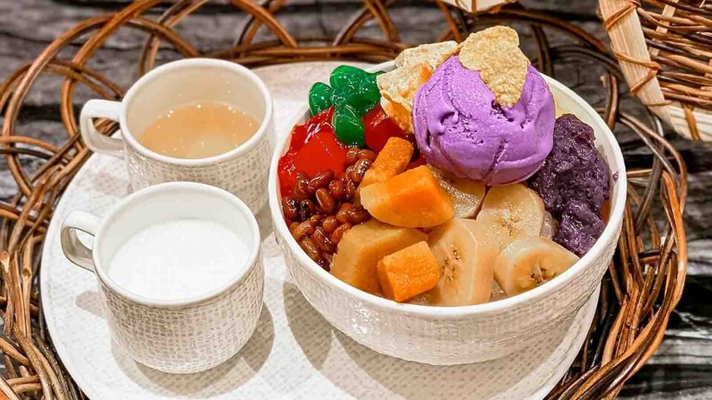 A bowl of halo-halo dessert next to two cups, with one of them being milk.