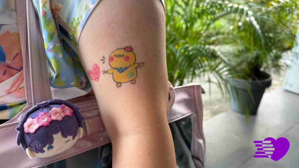 Photograph of Rafayel tattoo, an Artsby Birb on Melissa's left arm as she carries her Rafayel oshikatsu bag