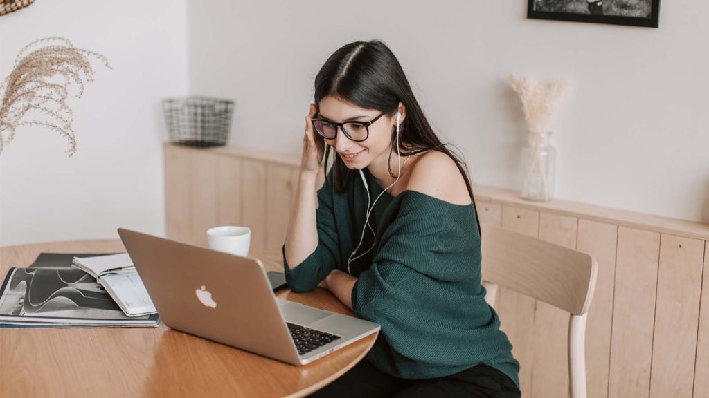 Smiling woman using laptop and earbuds for online learning in a cozy home setting.